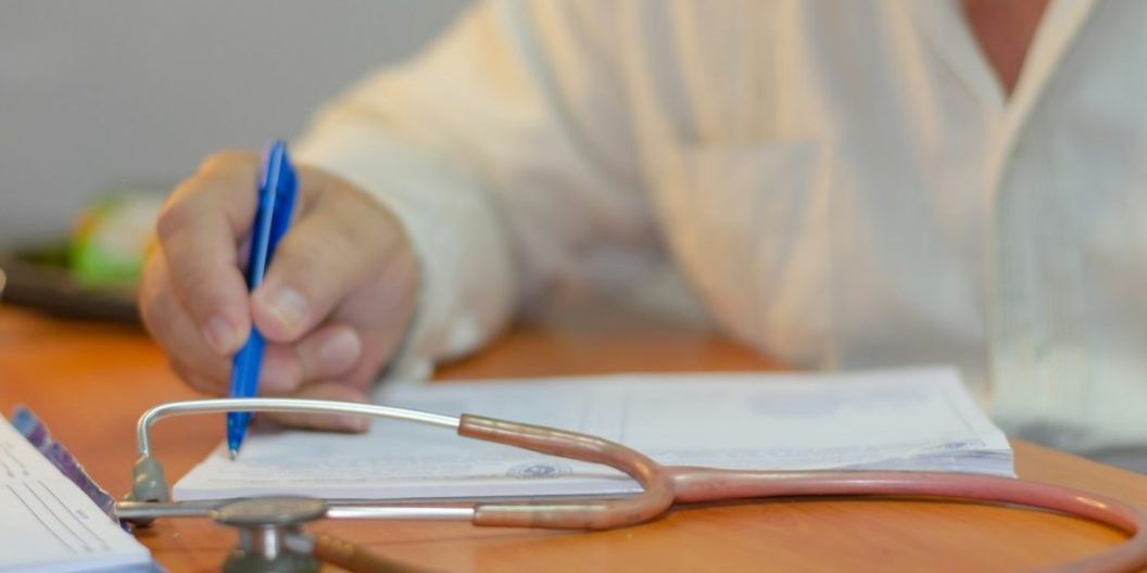 préconisations du médecin du travail une personne écrit sur un papier avec un stéthoscope au premier plan