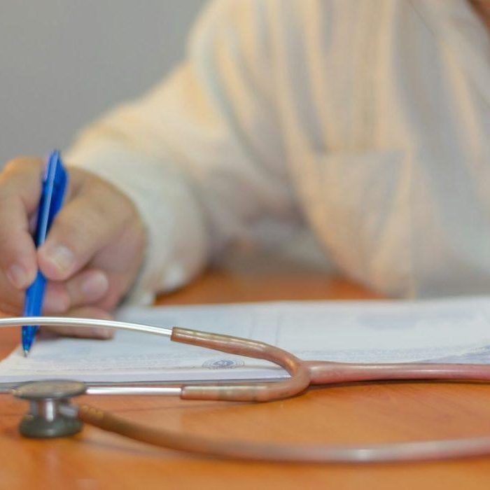 une personne écrit sur un papier avec un stéthoscope au premier plan